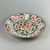 Angled view of antique hand-painted English platter with Arts and Crafts movement-inspired red, green, yellow, and pink floral motifs.