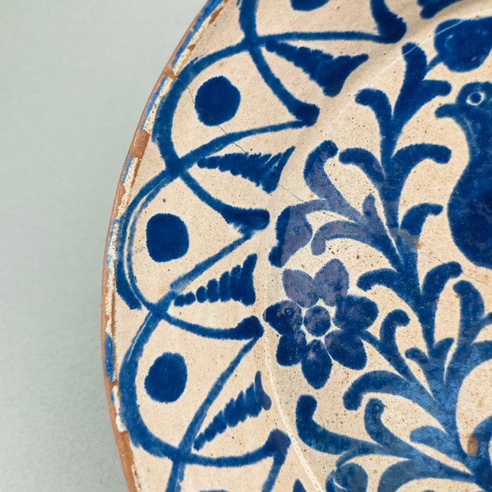 Glaze pooling and softened brushwork near the bowl's inner rim, showing the hallmarks of antique Andalusian pottery including age-worn edges, cobalt bleed, and freehand symmetry in floral scrolls.