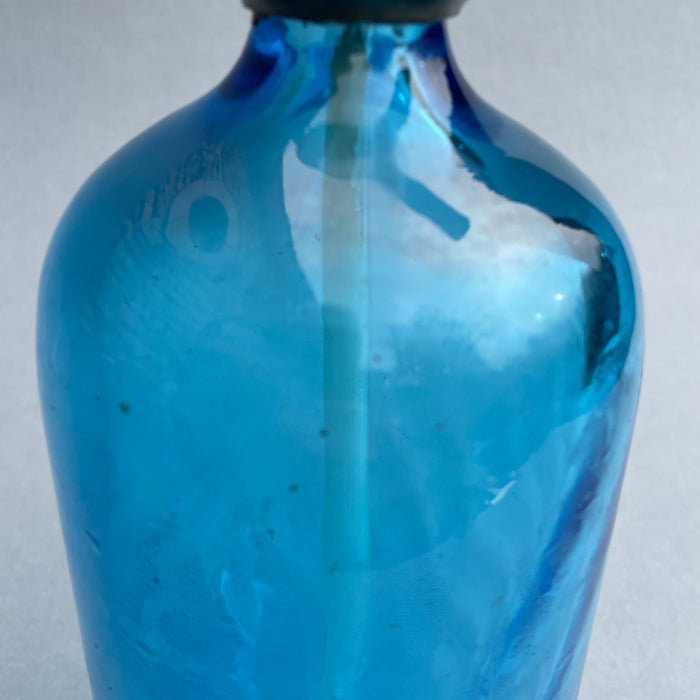Retro French café soda bottle with iconic metal tap and thick cobalt blue glass body, evoking prewar European design. Artistic detail of reflective cobalt glass surface, showing age-related marks and appealing color depth in this collectible barware piece.