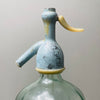 Unique collector’s piece with visible embossed script and aged coloration on top, appealing to lovers of vintage European glass. the bottle’s classic soda siphon shape and retro details like the ivory siphon lever and painted metal top.
