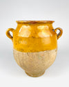 Antique French terracotta confit pot dating to the 19th century, with a rounded body, two curved loop handles and a rich mustard yellow glaze covering the upper half. The lower section retains exposed sandy beige earthenware with extensive surface patina, and the vessel stands on a small circular foot. A traditional French pottery jar with strong sculptural character, suited to French country decor.