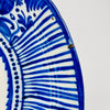 Cobalt blue Manises plate from 19th-century Spain, made in tin-glazed earthenware and painted with a central stylized botanical motif surrounded by dotted bands, fruit forms and tightly spaced radial stripes. Its saturated blue and cream palette makes the antique ceramic effective as Mediterranean wall art or Spanish pottery decor.