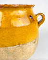Applied handle of an antique French yellow glazed pottery jar showing the thick curved terracotta loop, worn edges and small losses revealing the clay beneath the glaze. The surrounding mustard coloured surface contains firing marks, minute pits and fine crackling, characteristic details of this weathered confit vessel. An original utilitarian French ceramic object for farmhouse decor.