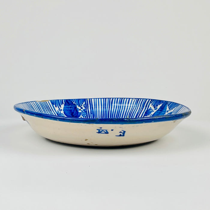 Large antique Spanish Manises plate in blue and white majolica, shown at human scale to convey its substantial decorative presence. The hand-painted cobalt design covers a deep earthenware charger with a central stylized flower, rhythmic striped border and traditional Valencian foliate ornament suited to a collected ceramic wall display.