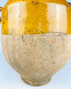 Antique French confit pot with a rounded body and an applied terracotta loop handle showing patches of worn golden glaze and exposed clay. The mustard yellow upper surface has fine crazing, small firing imperfections and the natural tonal variation of traditional pottery. The partially unglazed lower body reflects the practical construction of an old French preservation jar for French provincial decor.