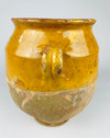 The opening of a 19th century French terracotta confit pot reveals concentric wheel throwing marks, darkened interior patina and areas of aged glaze. The thick circular rim has chips and irregular glaze losses exposing warm red clay, with two curved handles extending from the sides. This authentic antique French storage vessel has the weathered surface character sought for vintage home decor.