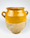 Surface detail of an antique French confit pot showing deep golden ochre glaze, fine interconnected crazing and small irregularities in the ceramic finish. Below the glazed section, the natural terracotta has developed a pale textured patina with areas of mineral staining and abrasion. The contrast between glossy colour and weathered clay makes this 19th century vessel suitable for wabi sabi decor.