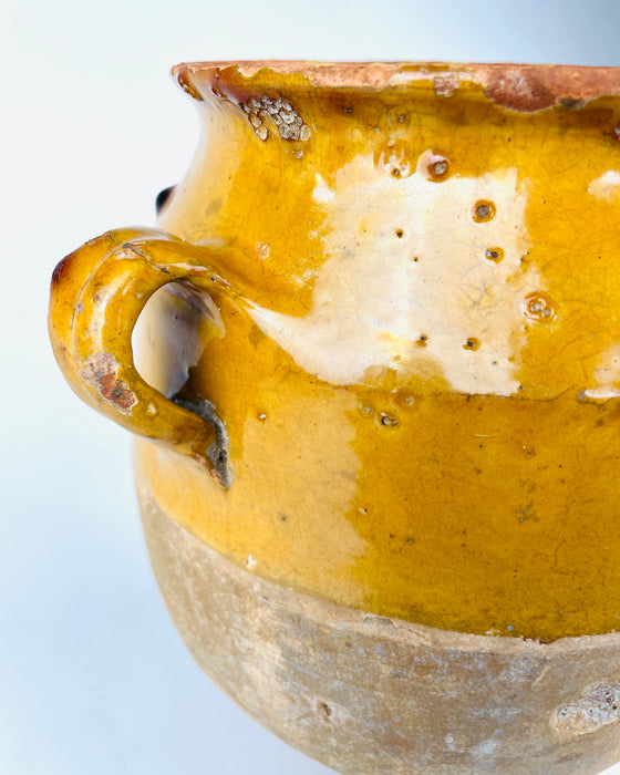 Antique French yellow glazed confit pot with a broad circular opening, gently flared mouth and two applied handles on opposite sides. The interior retains a muted olive ochre glaze with staining and throwing marks, while worn sections of the rim expose the reddish terracotta beneath. This traditional rural French pottery jar offers a substantial decorative form for cottage decor.