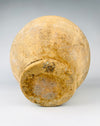 Underside of a 19th century French confit pot, showing a circular terracotta foot with extensive earthy patina, darker staining and a roughened exposed clay surface. The vessel has a rounded lower body that tapers into the narrow foot, supporting the traditional double handled storage form. This aged ceramic construction contributes to the object's distinctive character for wabi sabi decor.