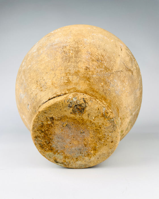 Underside of a 19th century French confit pot, showing a circular terracotta foot with extensive earthy patina, darker staining and a roughened exposed clay surface. The vessel has a rounded lower body that tapers into the narrow foot, supporting the traditional double handled storage form. This aged ceramic construction contributes to the object's distinctive character for wabi sabi decor.