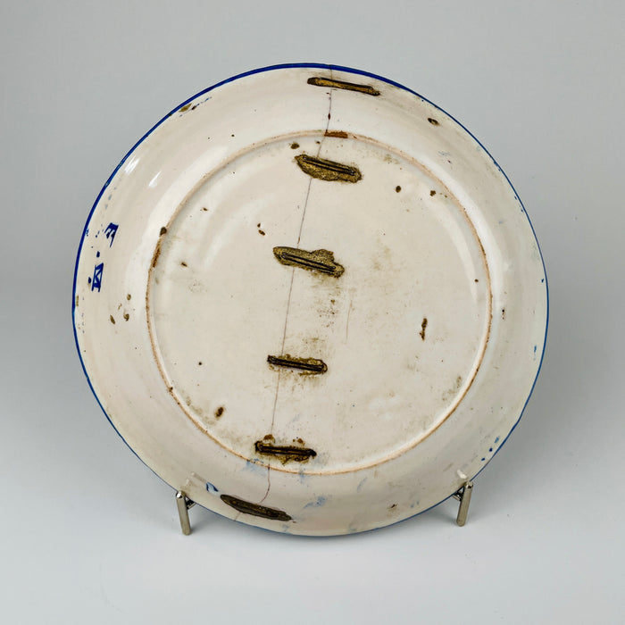 Underside of the antique Spanish Manises majolica plate showing a long historic break secured with multiple metal staples across the foot ring and body. The old repair joins the tin-glazed earthenware sections and forms an important part of the charger’s history, while the white reverse also retains kiln marks, wear and scattered glaze losses.
