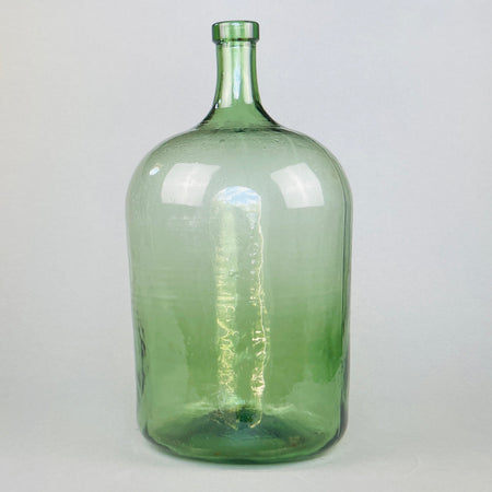 Full view of antique French green glass demijohn with elegant tall neck and handblown silhouette, standing upright against a neutral background.
