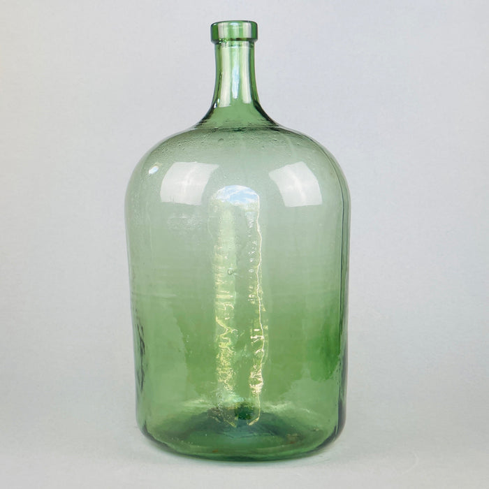 Full view of antique French green glass demijohn with elegant tall neck and handblown silhouette, standing upright against a neutral background.