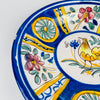 Pink five petal flower and sea green foliage hand painted across one compartment of the large Spanish majolica charger. Cobalt scrollwork, golden yellow bands and brown freehand outlines surround the floral panel, demonstrating the lively polychrome palette associated with Manises pottery and Mediterranean wall decor.