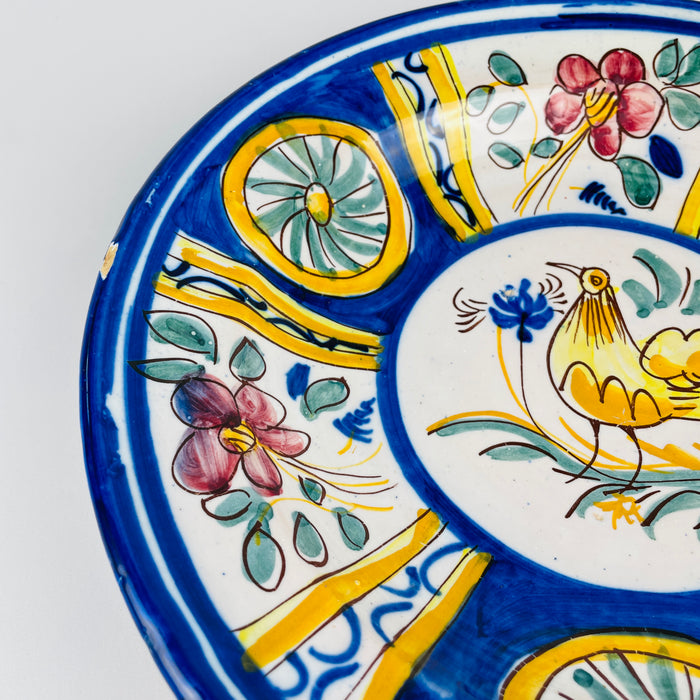 Pink five petal flower and sea green foliage hand painted across one compartment of the large Spanish majolica charger. Cobalt scrollwork, golden yellow bands and brown freehand outlines surround the floral panel, demonstrating the lively polychrome palette associated with Manises pottery and Mediterranean wall decor.