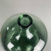 Light reflecting off the handblown green glass of the demijohn, showing authentic farmhouse design from mid-20th century France. French vintage glass wine vessel with tall, slim bottleneck and wide body, ideal for collectors or rustic interior décor.