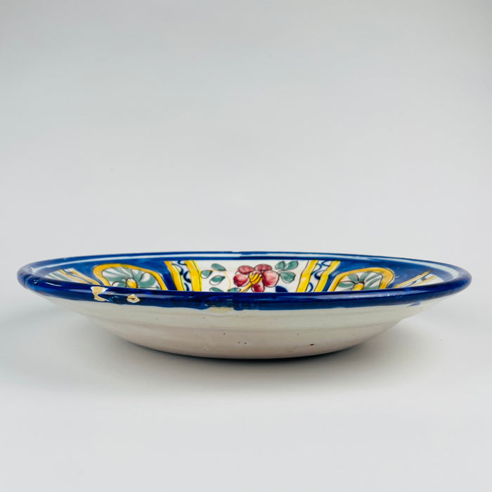 Decoration detail on the Spanish majolica charger showing a green spiral rosette enclosed by a golden yellow ring and deep cobalt blue field. Freehand brown outlines, visible brush variation and fine glaze lines record the handmade character of this circa 1900 Manises pottery wall plate and its folk art ceramic tradition.