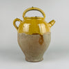Ceramic jar with yellow top and brown base on a white background. This image shows an antique French terracotta gargolette cruche pot from the 19th century, featuring a deep yellow glaze on the upper body and an unglazed lower half. The arched handle, side handle, and rounded spout highlight traditional French rural pottery craftsmanship. This large vessel adds warm natural texture to french country decor, farmhouse decor, cottage decor, and rustic home decor