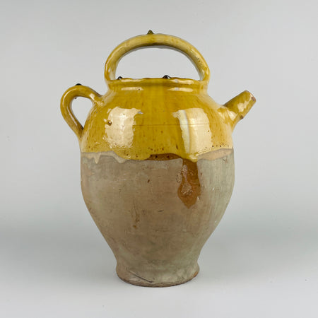 Ceramic jar with yellow top and brown base on a white background. This image shows an antique French terracotta gargolette cruche pot from the 19th century, featuring a deep yellow glaze on the upper body and an unglazed lower half. The arched handle, side handle, and rounded spout highlight traditional French rural pottery craftsmanship. This large vessel adds warm natural texture to french country decor, farmhouse decor, cottage decor, and rustic home decor