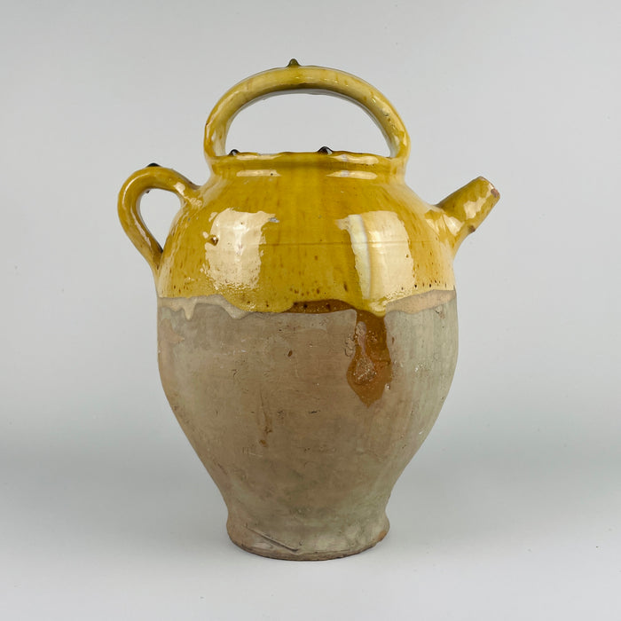 Ceramic jar with yellow top and brown base on a white background. This image shows an antique French terracotta gargolette cruche pot from the 19th century, featuring a deep yellow glaze on the upper body and an unglazed lower half. The arched handle, side handle, and rounded spout highlight traditional French rural pottery craftsmanship. This large vessel adds warm natural texture to french country decor, farmhouse decor, cottage decor, and rustic home decor