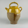 Side profile of a large antique French terracotta cruche pot shows its curved shoulder, yellow glazed surface, and spout used historically for pouring water or wine. The pot’s aged surface displays natural wear consistent with 19th century use. This handcrafted French pottery piece enhances farmhouse decor, cottage decor, rustic home decor, french country decor, and mediterranean decor, especially in rooms where warm terracotta tones are desired.