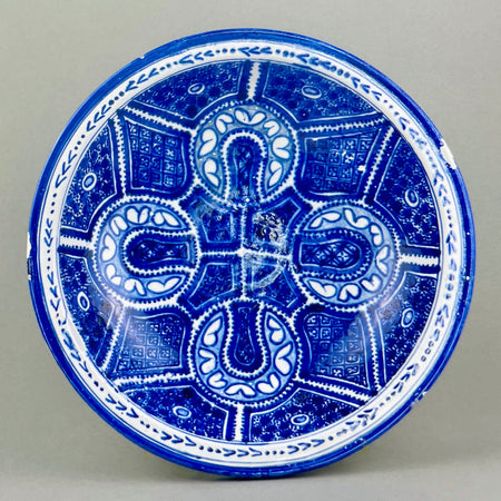 Overhead view of vintage Moroccan ceramic bowl showing hand-painted blue geometric design on white glaze with radial symmetry.