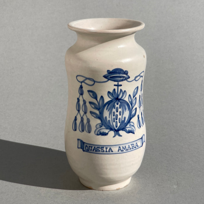 Close-up of the "Quassia Amara" inscription on a Talavera pottery jar, with detailed brushwork and baroque botanical flourishes, used to label traditional herbal remedies in antique apothecaries.