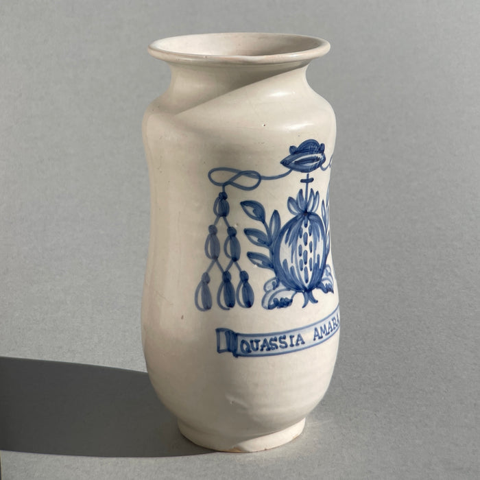 Spanish majolica pharmacy jar, hand-painted with pomegranate fruit and foliage, inscribed “Quassia Amara,” referencing the bitter medicinal plant once used in tonic preparations.