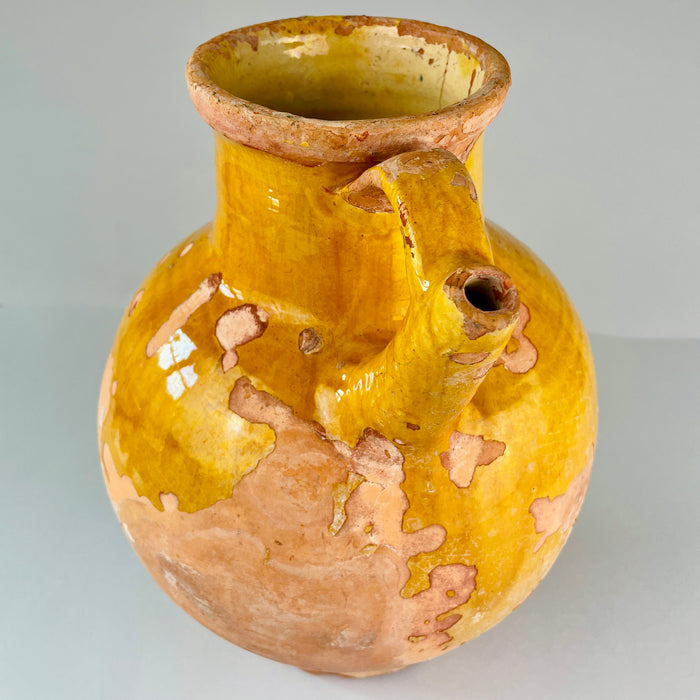 Yellow ceramic vase with brown patches on a gray background. Highlight on glaze losses and exposed terracotta surface of antique French jug, emphasizing texture, earthy tones, and aged patina, making it ideal for styling in wabi-sabi or Mediterranean-inspired home décor.