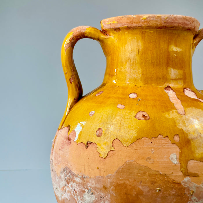 Yellow ceramic vase with brownish patina on a gray background. Detailed close-up of gargolette handle and spout, with glaze loss and earthy patina visible, emphasizing the jug’s utilitarian past and suitability for wabi-sabi interiors that value aged authenticity and artisanal imperfections.