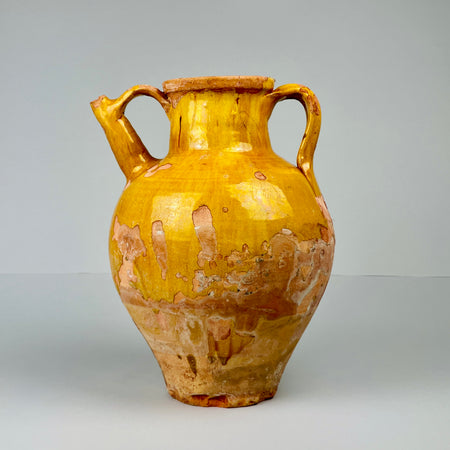 Antique French terracotta gargolette jug with ochre-yellow glaze, showing worn areas revealing natural clay beneath, photographed upright against neutral background, highlighting its rustic farmhouse charm and 19th-century craftsmanship.