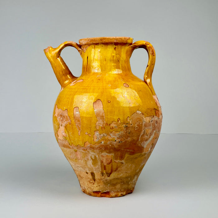 Antique French terracotta gargolette jug with ochre-yellow glaze, showing worn areas revealing natural clay beneath, photographed upright against neutral background, highlighting its rustic farmhouse charm and 19th-century craftsmanship.