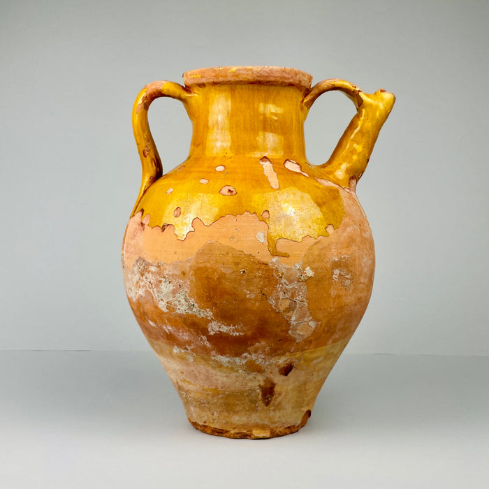 Antique ceramic jar with a yellowish-brown glaze on a gray background. Full frontal view of antique gargolette jug with ochre glaze partially covering terracotta surface, showing rounded belly and narrow rim, perfect for rustic French farmhouse or Mediterranean-style home decoration.