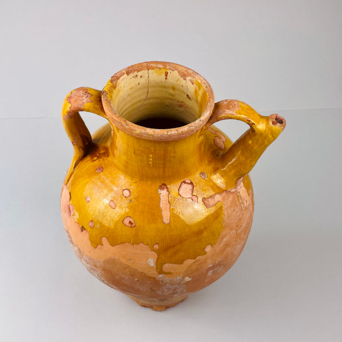 Terracotta vase with two handles on a light gray background. Antique French gargolette jug with spout, photographed in side angle against plain background, demonstrating balanced proportions, strong handles, and ochre glaze, perfect for collectors of French rustic pottery.