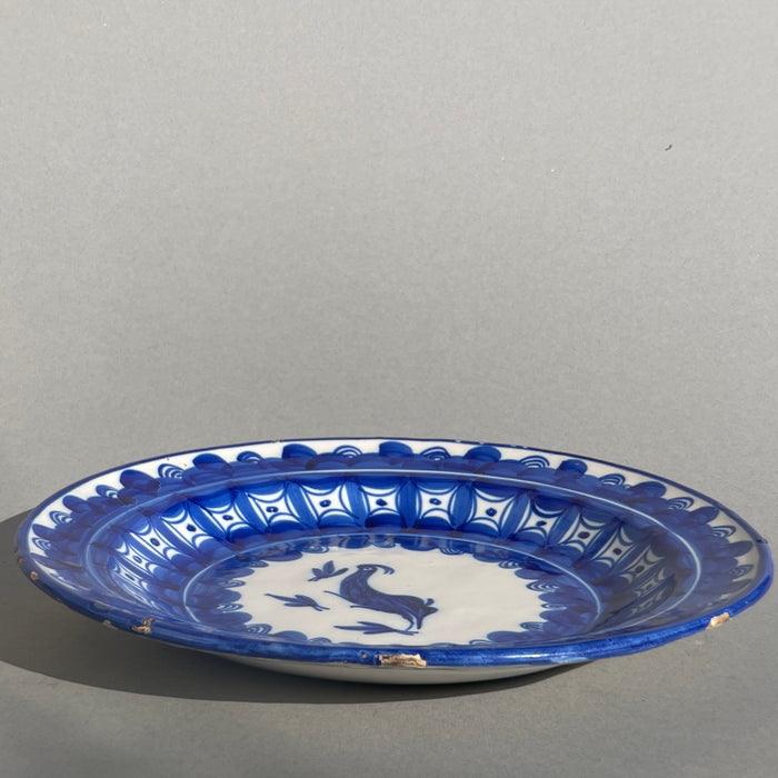 Blue and white Spanish wall plate photographed in full sun, capturing the high-contrast visual appeal for rustic, coastal, or wabi-sabi interiors. Handcrafted blue and white Manises ceramic plate placed in daylight, highlighting glaze reflections and natural imperfections from historical firing.