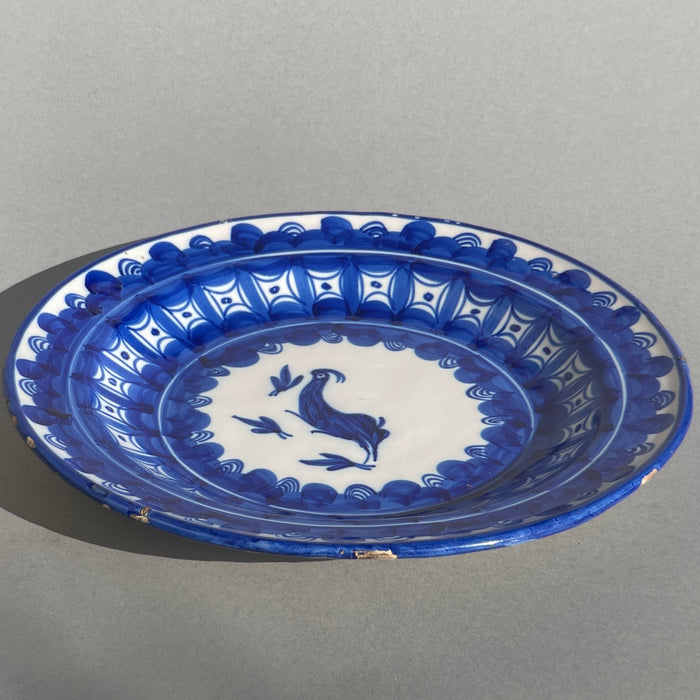 Close-up of the Manises plate’s center featuring a stylized bird surrounded by brush-painted foliage, showcasing traditional Spanish faience techniques in rich cobalt glaze.