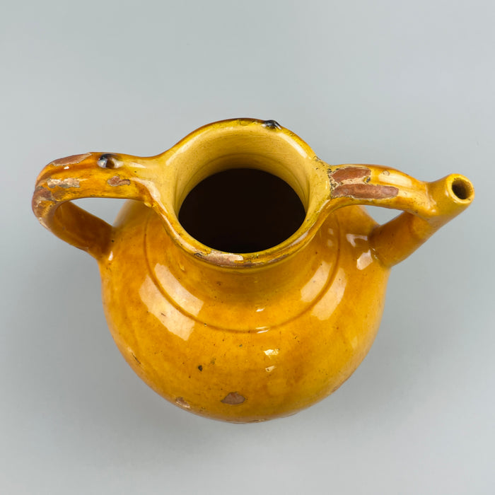 Warm light image of antique French jug with golden glaze reflecting softly, showing its authentic patina, chipped surface, and rounded form, ideal for farmhouse interiors, ceramic enthusiasts, or collectors of French pottery.