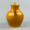 Close-up detail of yellow-glazed antique French jug showing curved handle and pouring spout, with visible glaze variation and fine patina, highlighting hand-thrown craftsmanship and its suitability for country kitchen or vintage shelf styling.