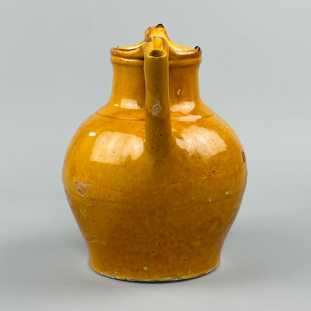 Close-up detail of yellow-glazed antique French jug showing curved handle and pouring spout, with visible glaze variation and fine patina, highlighting hand-thrown craftsmanship and its suitability for country kitchen or vintage shelf styling.