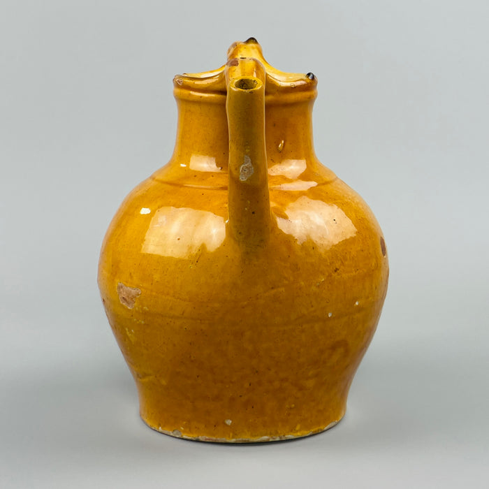 Close-up detail of yellow-glazed antique French jug showing curved handle and pouring spout, with visible glaze variation and fine patina, highlighting hand-thrown craftsmanship and its suitability for country kitchen or vintage shelf styling.