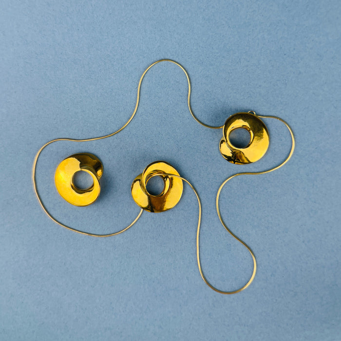 Sculptural pendant by Laragh Stuart in 14k gold-plated bronze, created through lost-wax casting from a hand-carved wax model. Its organic circular form with asymmetrical opening reflects minimalist design principles while serving as both jewelry and wearable sculpture. 
