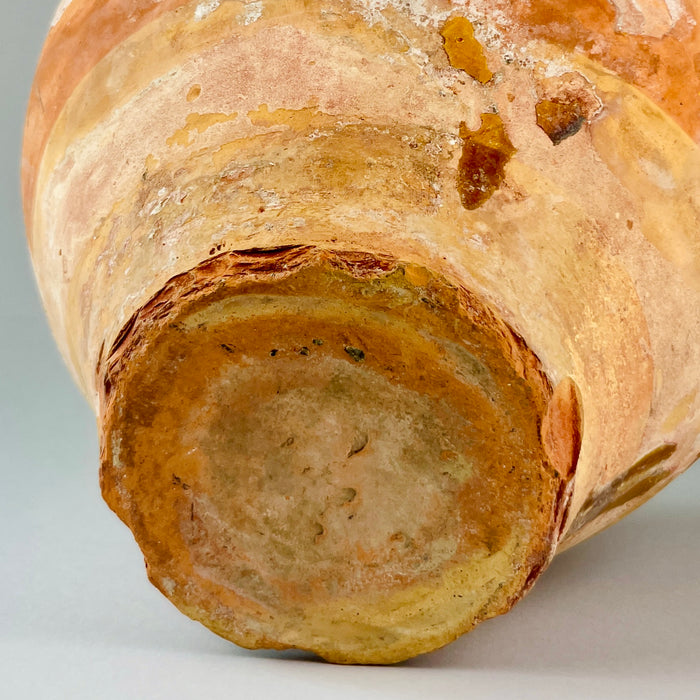 Close-up of a textured ceramic vase on a gray background. Bottom view of antique terracotta jug showing unglazed base with signs of wear and mineral deposits, confirming its 19th-century origin and authentic handcrafted nature typical of rural French pottery traditions.
