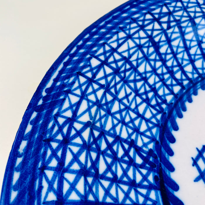 Spanish majolica plate from Manises with a signed painted mark, a white glazed ground, and bold cobalt ornament. Overlapping brush lines form a complex field of triangles and diamonds around the rim, while the center remains open around a stylized plant. The large antique charger brings graphic blue and white decor to a wall or display stand.