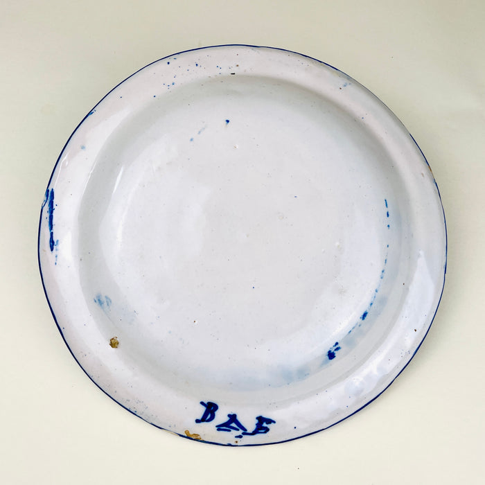 Antique cobalt Manises plate showing the direct hand of the decorator through variations in brush pressure, line width, and glaze saturation. The white earthenware ground is covered by a dense geometric lattice around the rim and a restrained central composition of botanical and grid symbols. The signed Spanish wall plate retains rim chips and fritting.