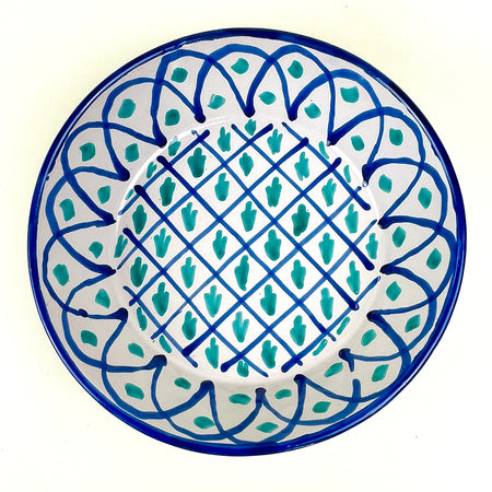 Large Spanish Fajalauza lebrillo bowl from Granada pottery tradition, hand painted in cobalt blue and green on a cream-white glazed earthenware surface. The deep ceramic bowl has a lattice center, vegetal motifs, blue arched border, and pierced hanging hole for wall display in Mediterranean decor or Spanish farmhouse decor.