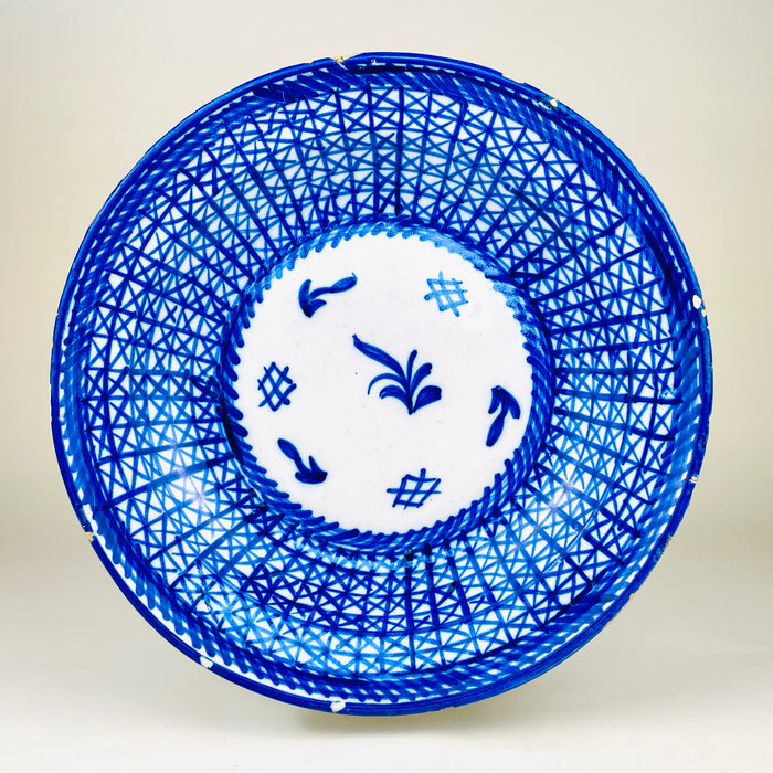 Antique Spanish majolica plate from Manises, Valencia, signed and hand painted in cobalt blue over a white tin glazed earthenware ground. The large charger has a dense crosshatched lattice across the broad sloping rim, braided blue borders, and a central reserve with stylized botanical and grid motifs, making it distinctive ceramic wall art for Mediterranean decor.