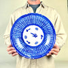 Hand painted blue charger from Manises, Spain, formed in glazed earthenware with a wide sloping rim and low profile. Cobalt lines overlap into triangular and diamond shapes that resemble woven basketry, while the white center carries simplified plant and grid motifs. The signed antique plate is suited to ceramic wall art and collected Spanish pottery.