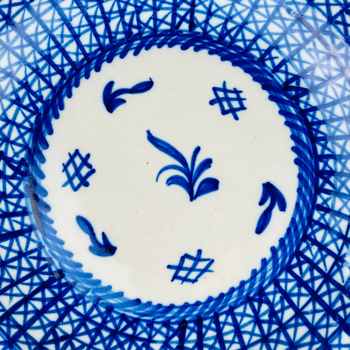 Antique blue and white Manises plate with a signed mark and hand applied cobalt decoration. The geometric border varies in line weight, spacing, and pigment intensity, showing the individual brushwork behind the design. Scattered rim fritting, chips, and exposed earthenware preserve the aged character of this large Spanish majolica wall plate.