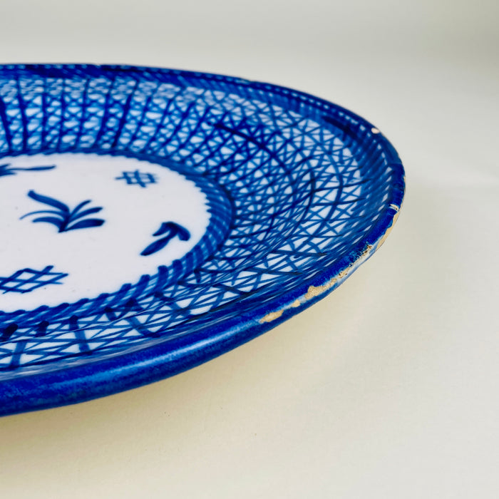 Large cobalt blue Manises charger made in Spain from tin glazed earthenware and individually decorated by hand. The broad shallow form is framed by strong blue edging and a geometric network of lines, with small areas of rim loss revealing the ceramic body beneath. Its signed early 20th century character makes it collectible ceramic wall art.