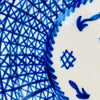 Antique Manises pottery charger made from tin glazed earthenware and painted in cobalt blue with an intricate geometric lattice. The broad border is built from overlapping diagonal, vertical, and radial lines, framed by darker blue bands around the rim and center. Small edge chips and glaze losses remain visible on this signed Spanish ceramic wall art.